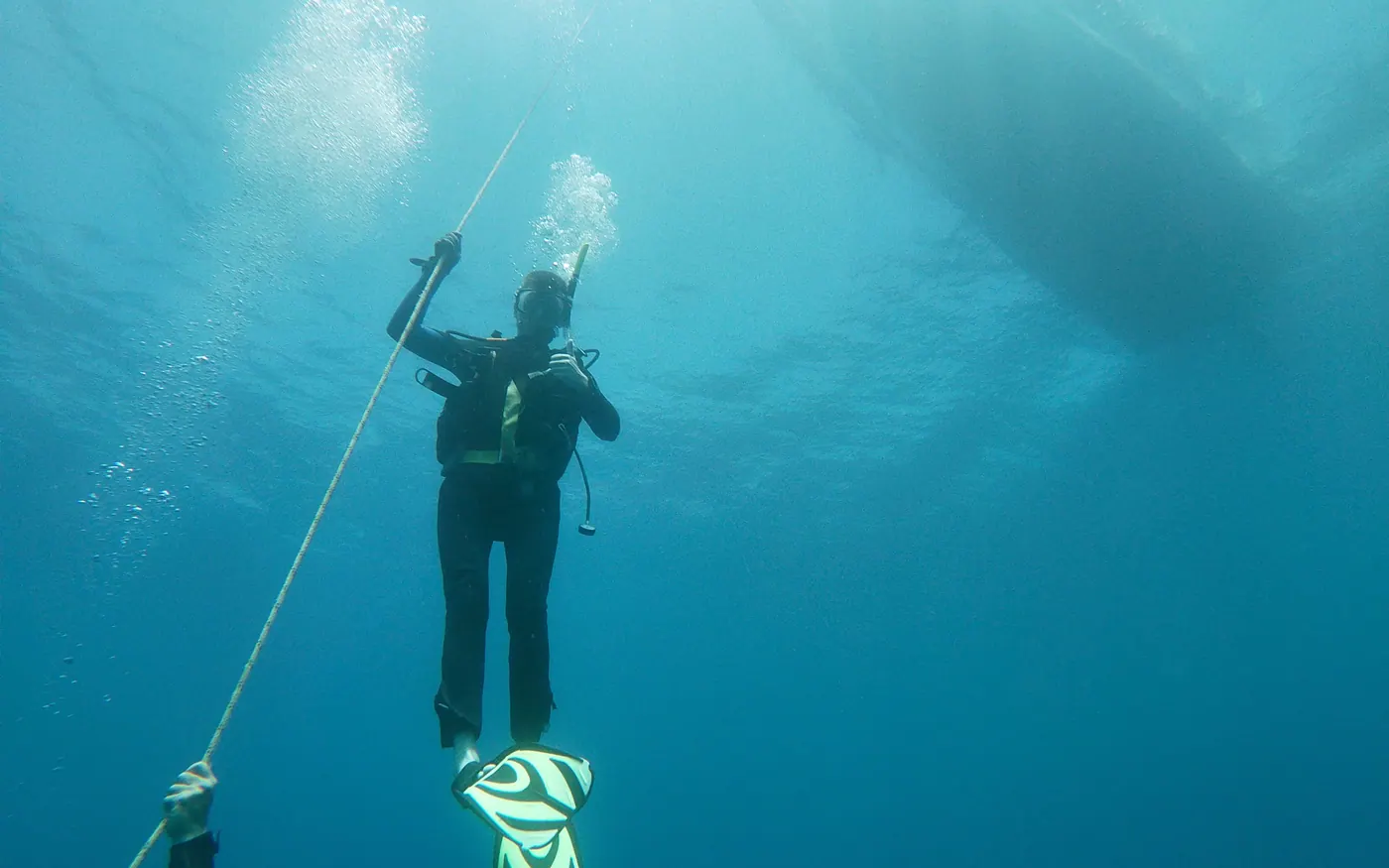 A scuba diver ascending a line beneath a boat hull