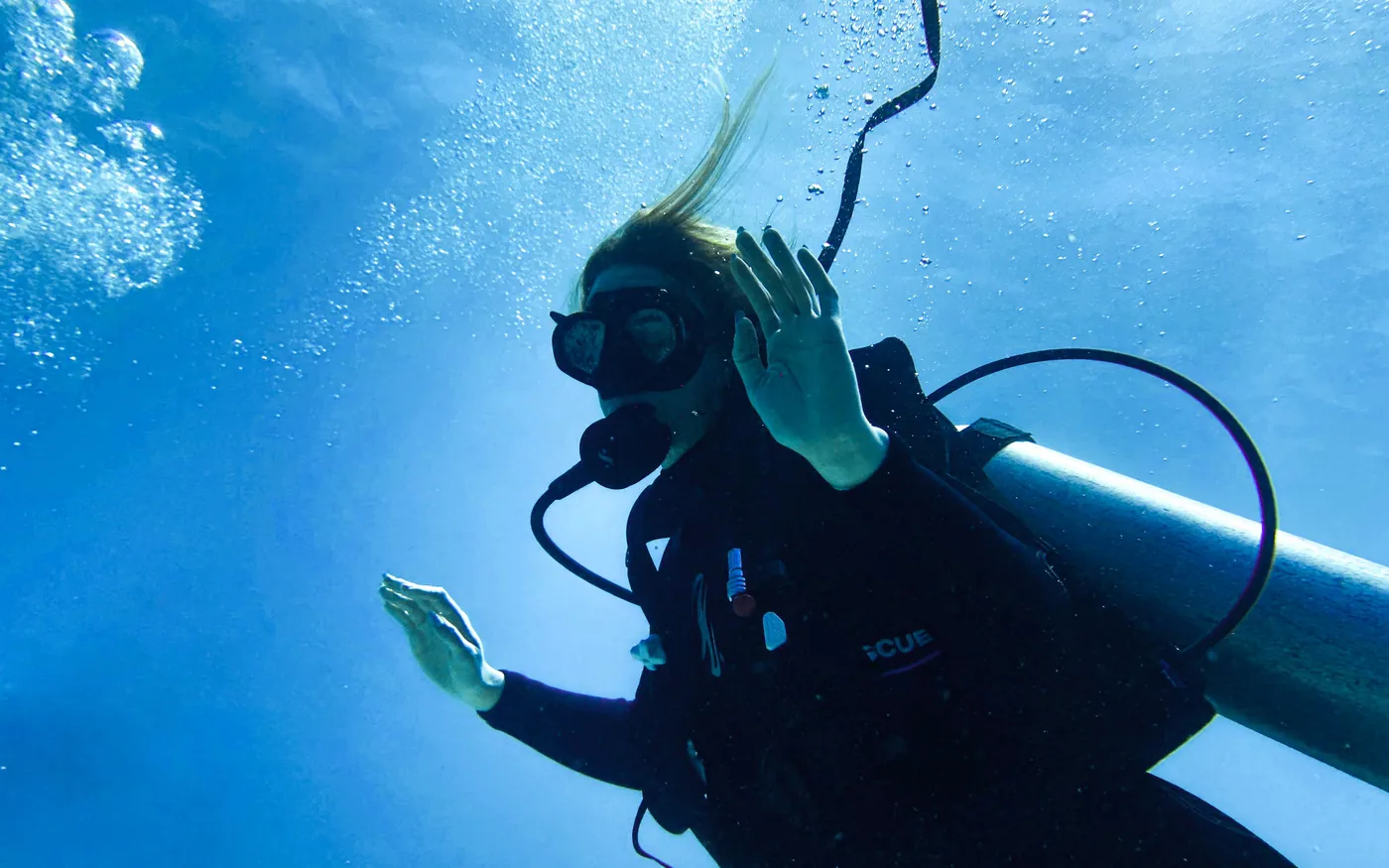 A scuba diver ascending with one hand raised above the head