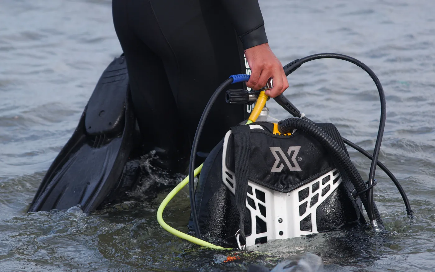 A diver in a wetsuit carrying a BCD and regulator out of the water