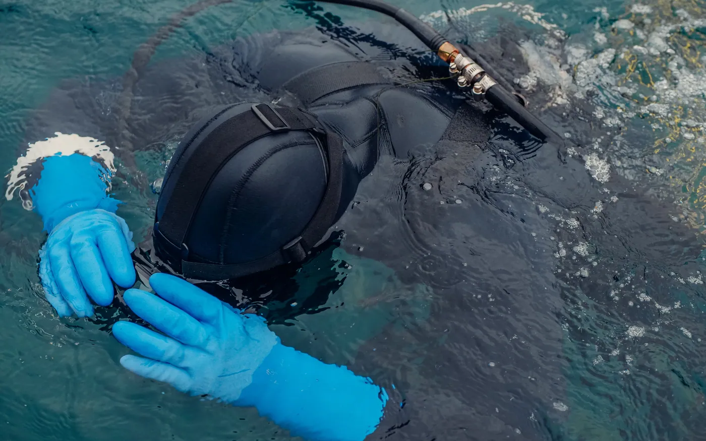 A diver at the surface adjusting a mask with gloved hands