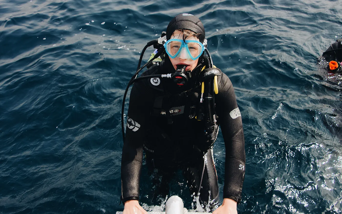 A scuba diver at the surface climbing a boat ladder after a dive