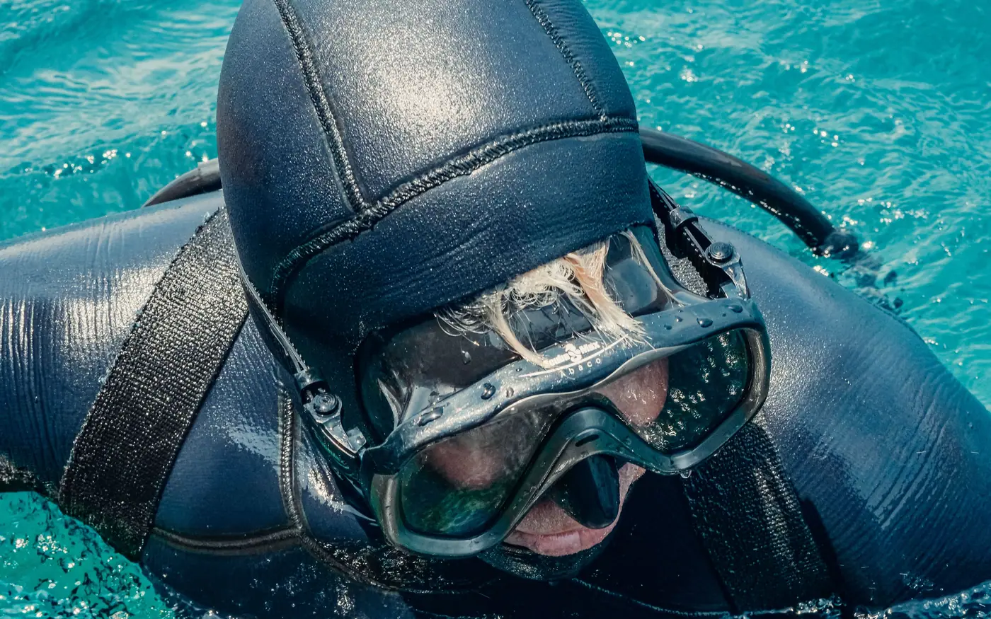 A diver's face framed by a tight neoprene hood and mask