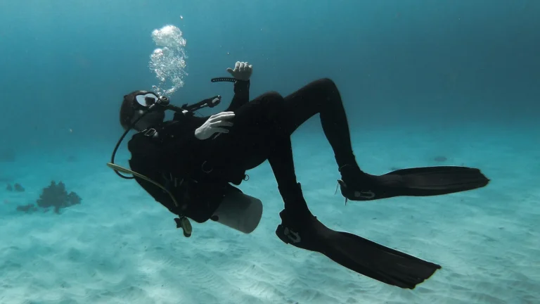 A scuba diver swimming flat and horizontal a few feet above a sandy bottom