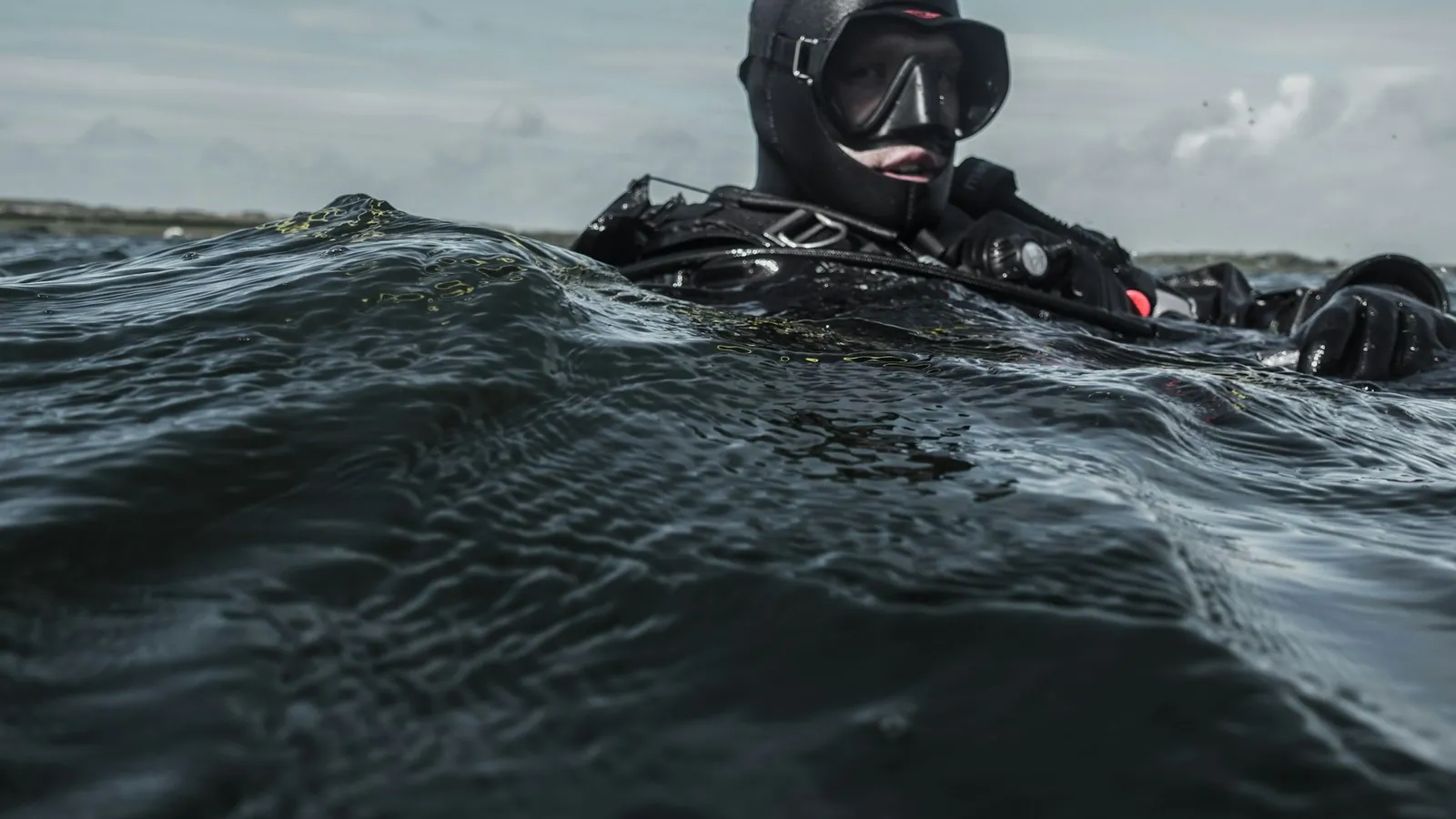 A diver in a hood and mask at the surface in cold grey water