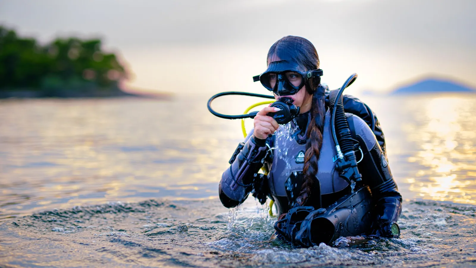 A scuba diver in full kit wading into the water from shore at dusk