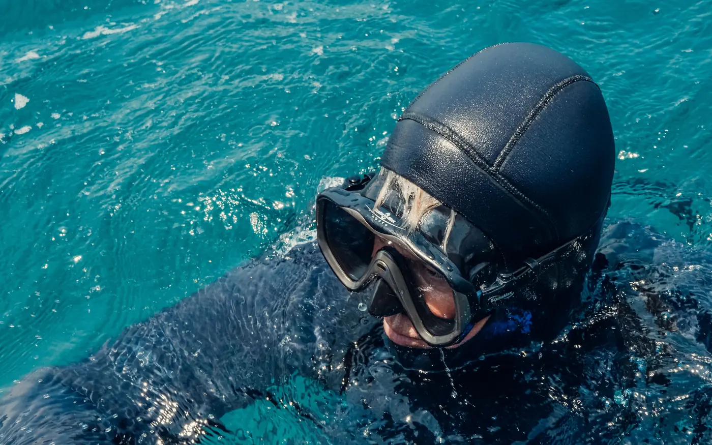 Close-up of a scuba diver in a hood and mask at the surface in dark water