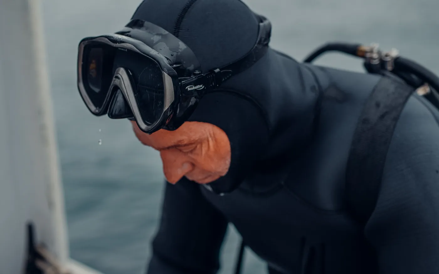 A diver in a black hooded wetsuit and mask preparing on a boat