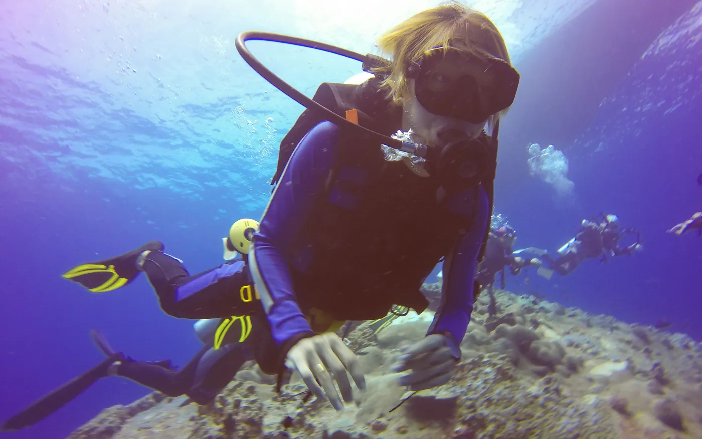 A scuba diver on a reef with the shoulder straps and inflator of a buoyancy device visible