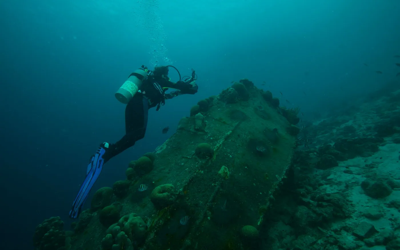 A scuba diver swimming above a wreck in green coastal water