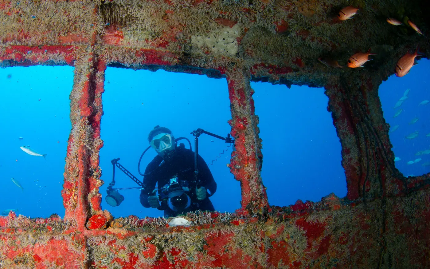 A scuba diver with a light framed in the window openings of a shipwreck