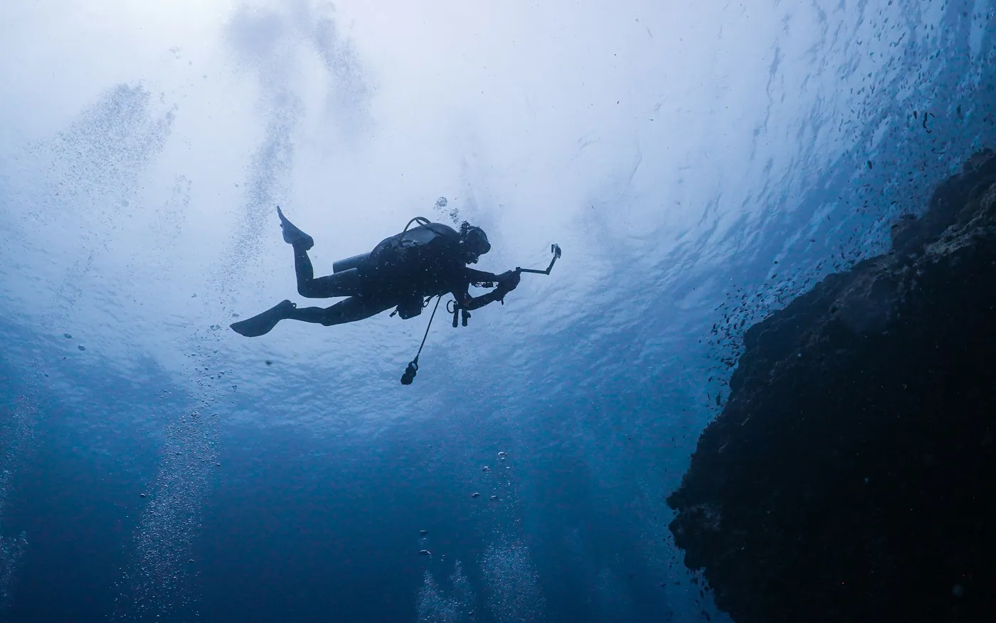 A scuba diver silhouetted against the surface beside a wall