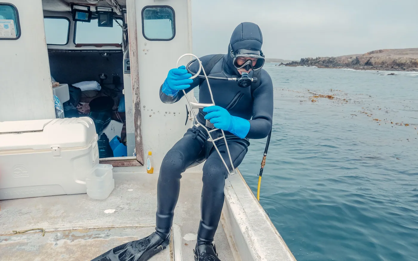 A diver in a hooded wetsuit sitting on the gunwale of a boat before entering