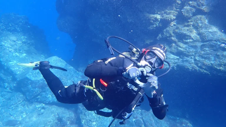 A scuba diver in open blue water with cylinders and regulator hoses visible