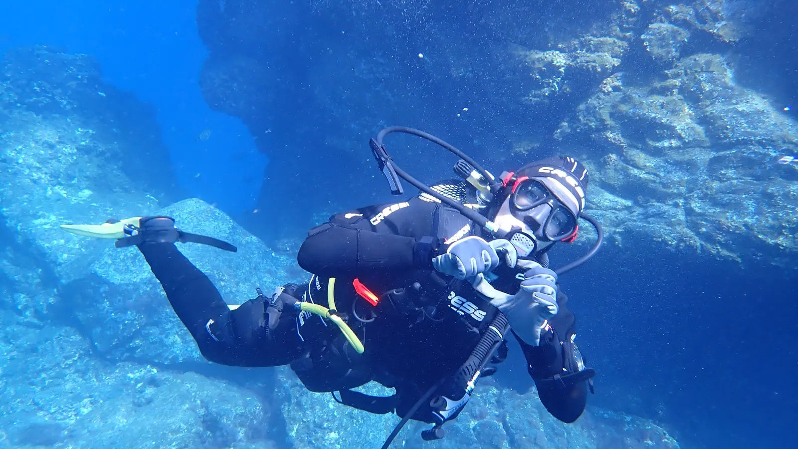 A scuba diver in open blue water with cylinders and regulator hoses visible