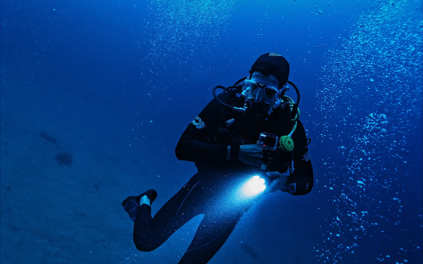 A scuba diver carrying a dive light in deep blue water