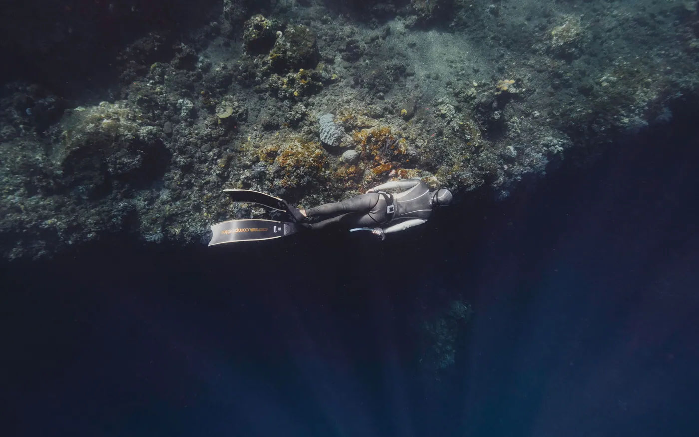 A scuba diver moving slowly along a wall in dim water