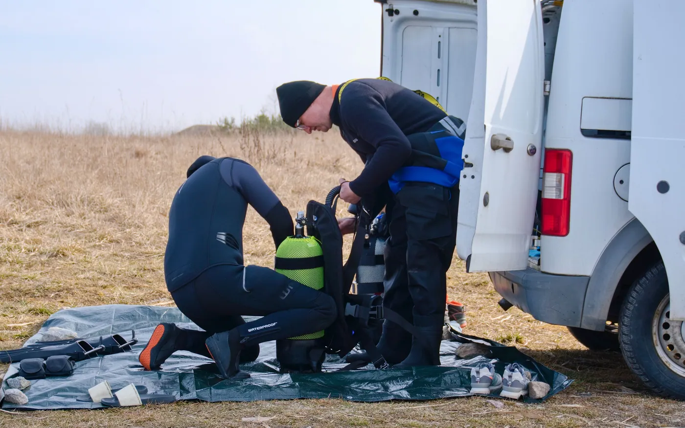 Two divers assembling their own scuba gear beside a van before a dive