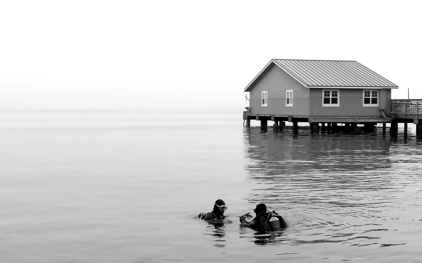 Two scuba divers at the surface in calm water near a boathouse