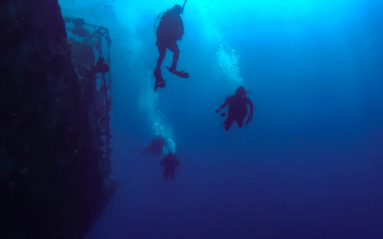 Three scuba divers descending along a steep underwater wall