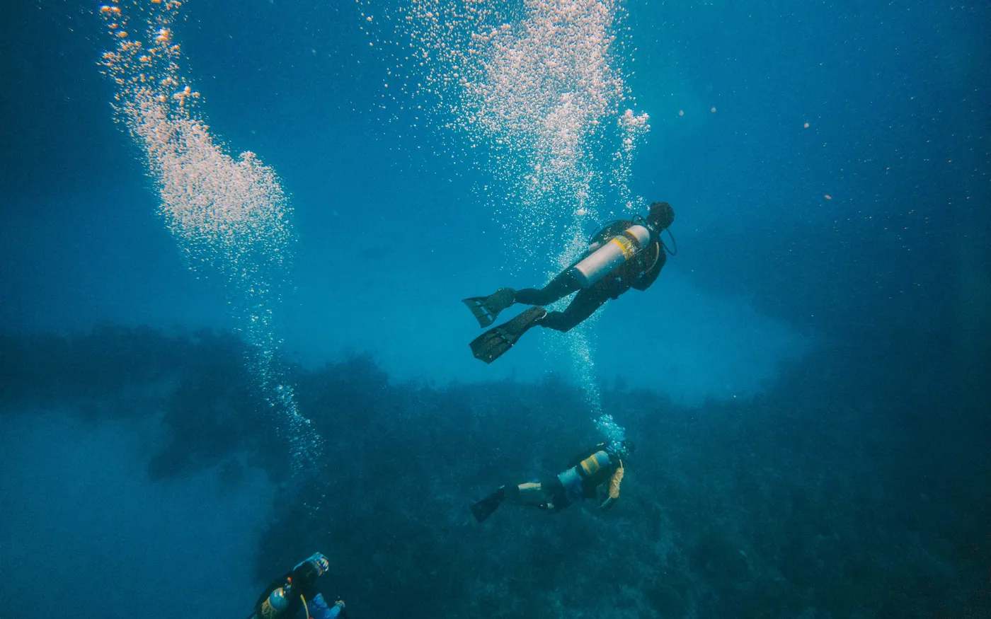 Three scuba divers descending in loose formation over a reef
