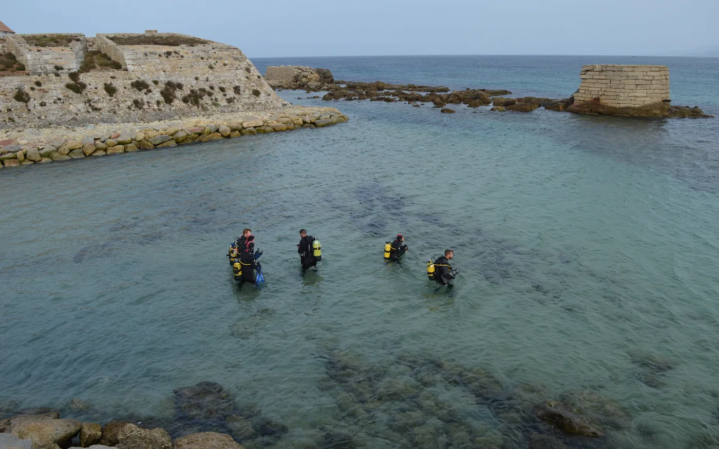 A group of divers walking into the water from a rocky shore entry