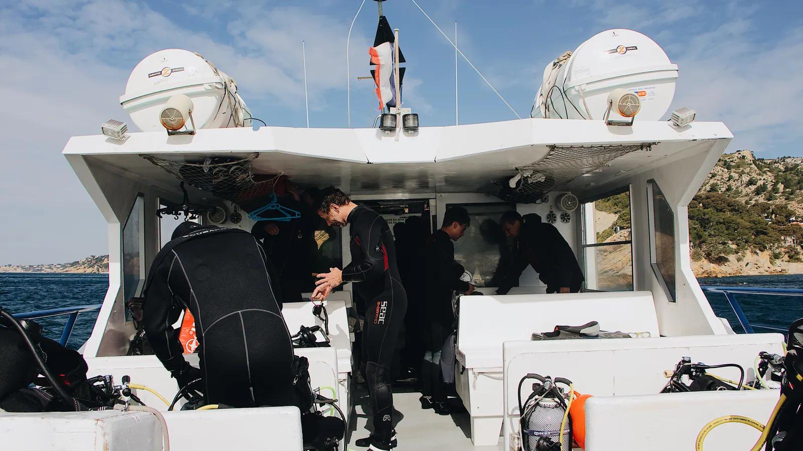 Divers in wetsuits assembling cylinders and BCDs on the deck of a dive boat