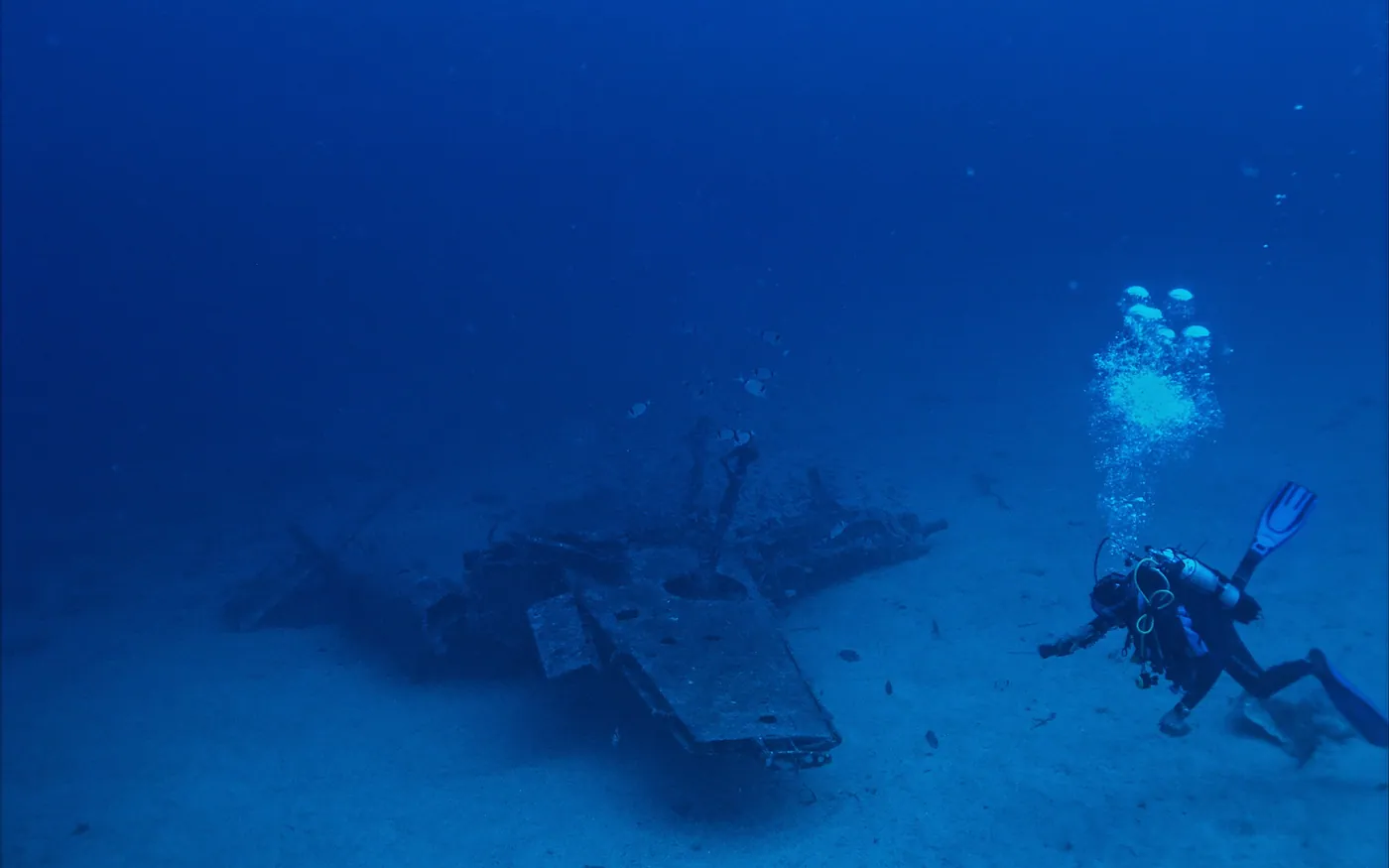 Two scuba divers swimming above a wreck on a sandy bottom