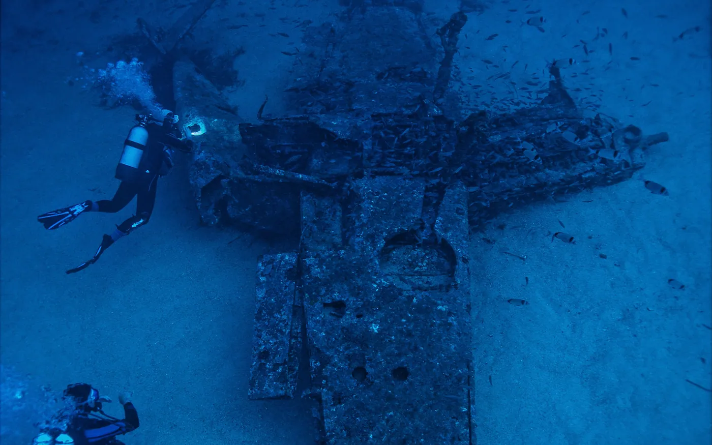 Two scuba divers above the wreck of an aircraft on a sandy bottom