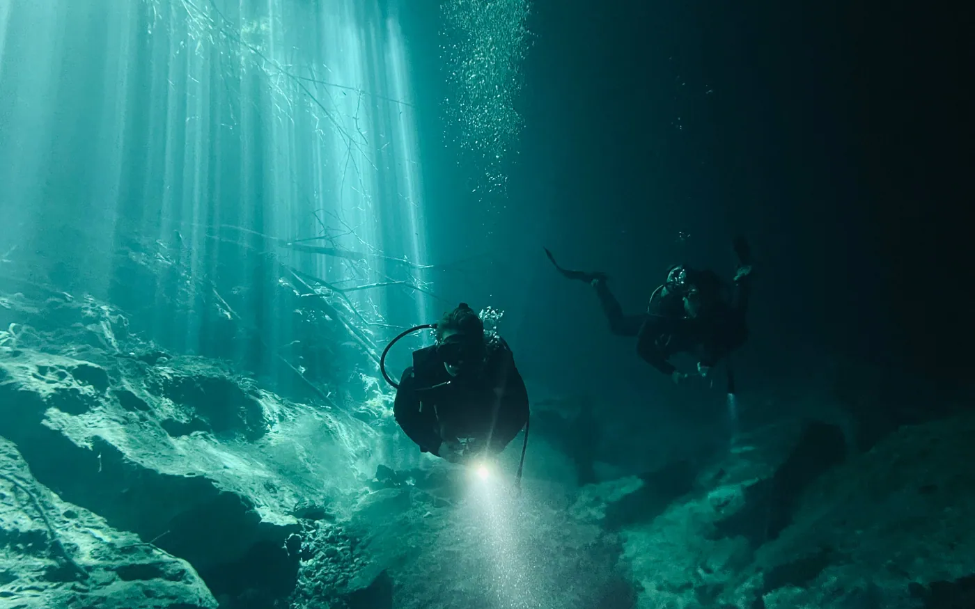 Two scuba divers using a dive light in dark green water