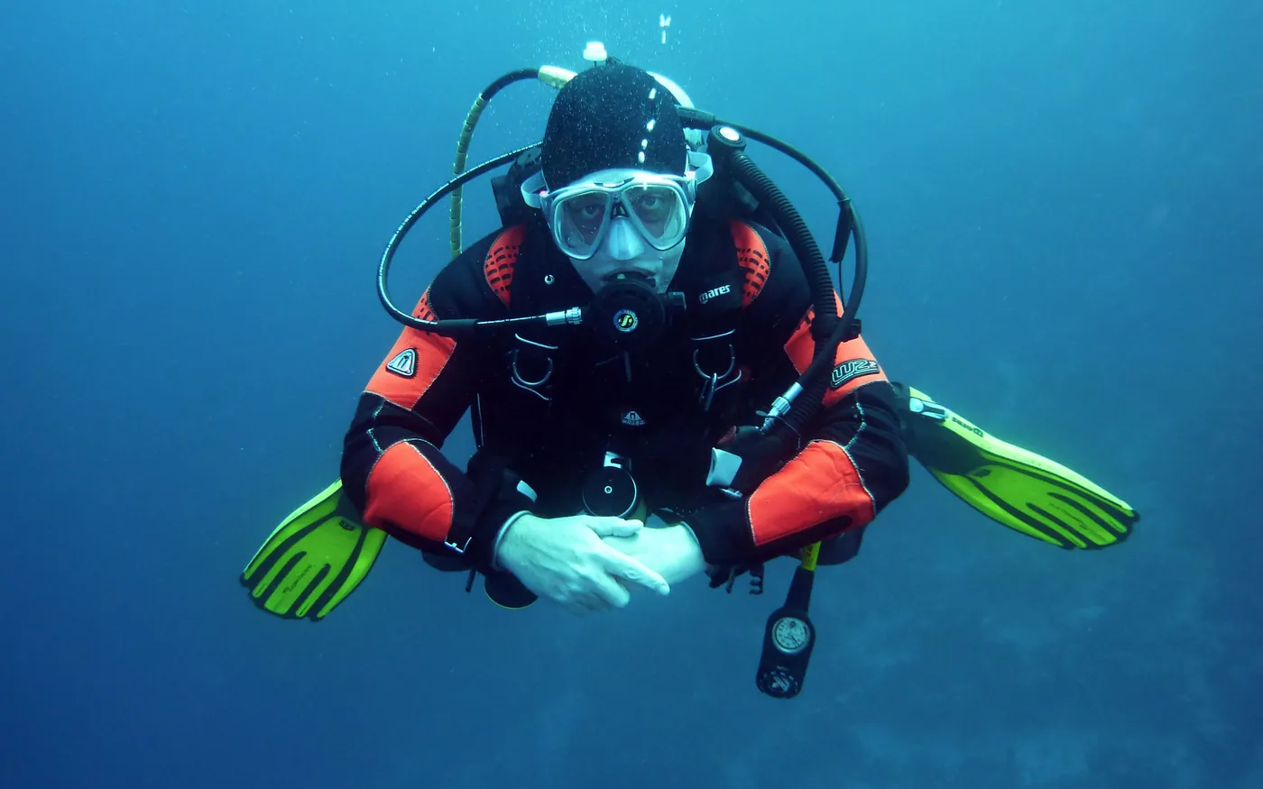 A diver in a drysuit swimming underwater with bright fins