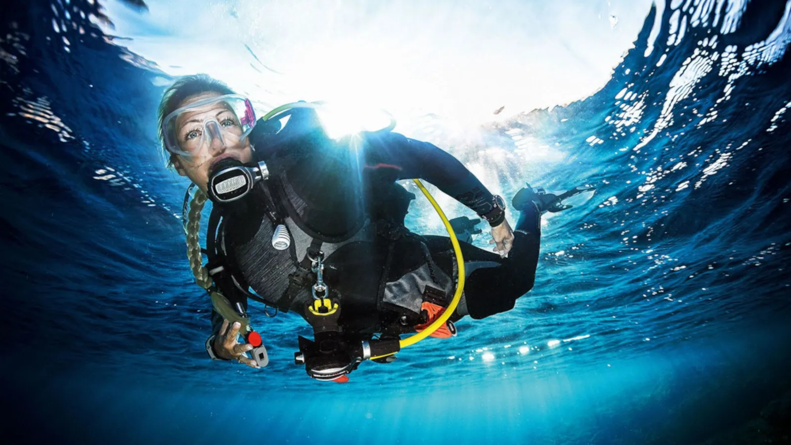A scuba diver just below the surface with sunlight breaking overhead