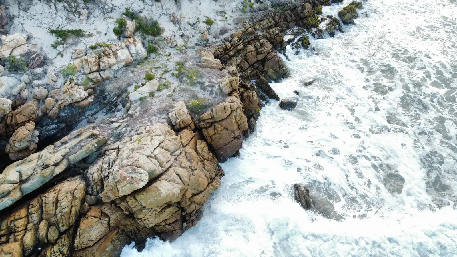 Surf breaking against a granite headland seen from above