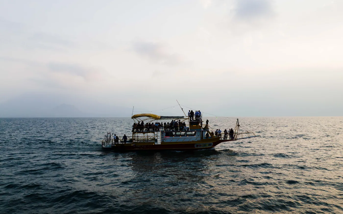 A boat carrying a group of people heading out across flat water at dawn