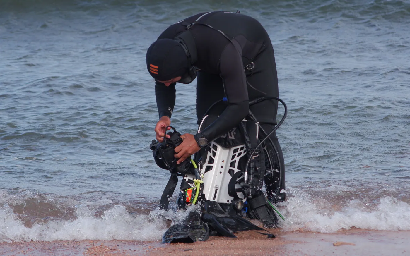 A diver assembling gear at the water's edge in light surf