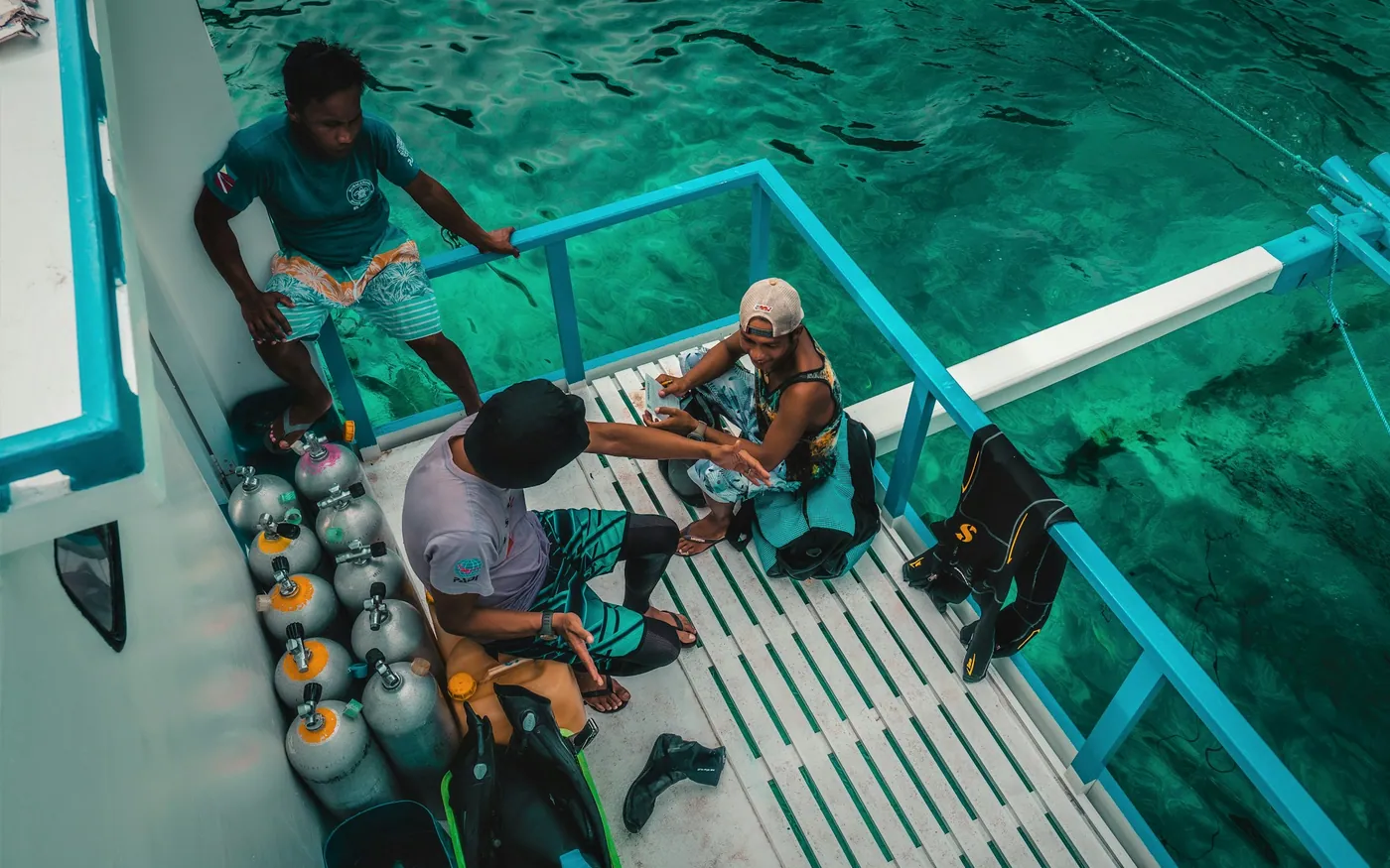 Divers kitting up on the dive platform of a boat with cylinders racked behind