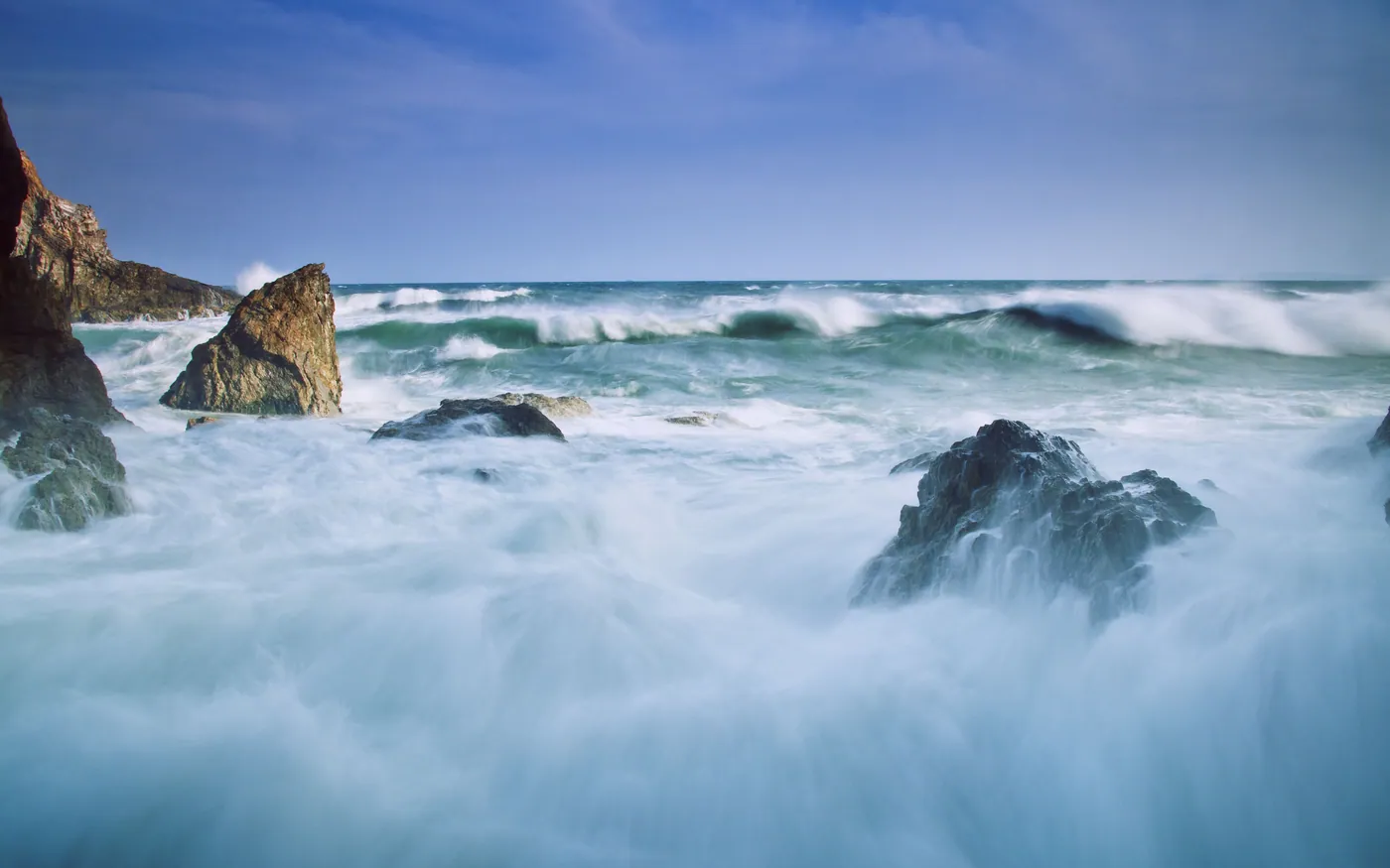 A long exposure of surf washing over shoreline rocks