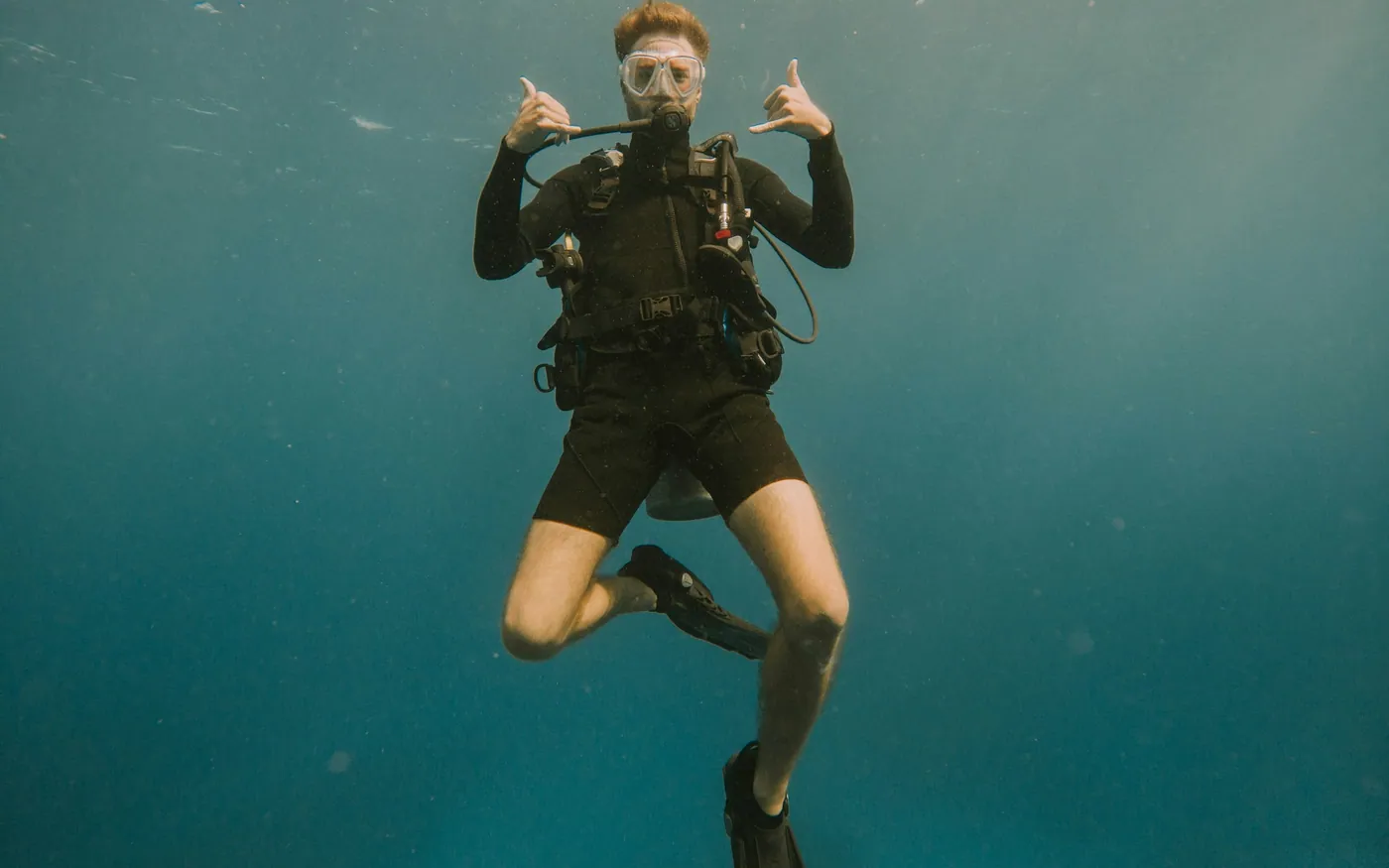 A diver in full scuba gear giving an OK signal in clear water