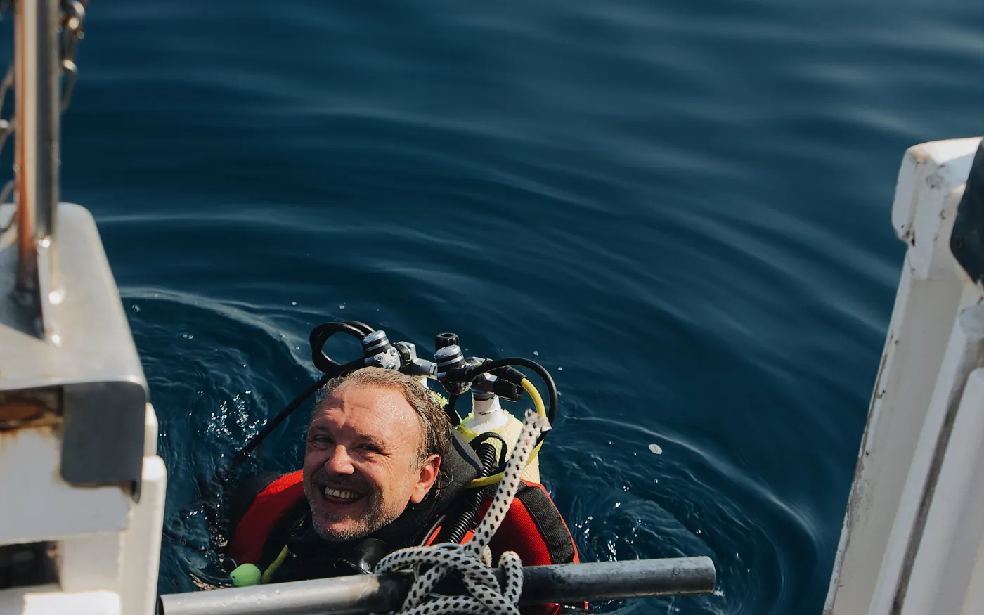 A smiling scuba diver at the surface beside a dive boat after a dive