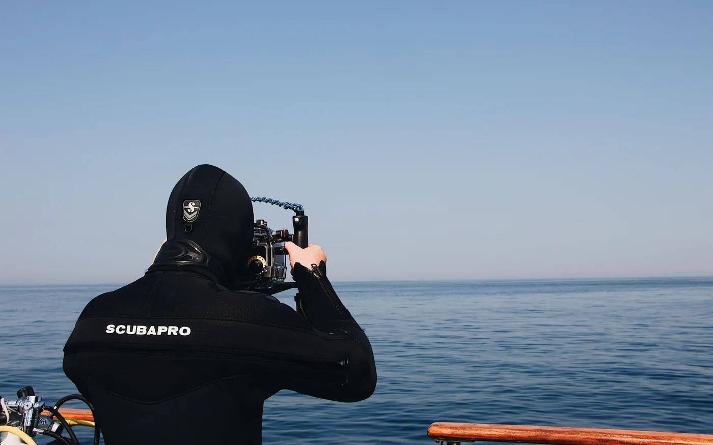 A diver in a hood carrying an underwater camera rig on a boat