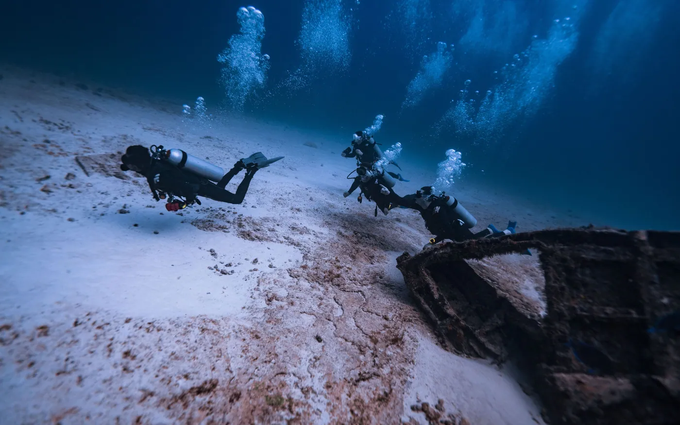 Two divers photographing wreckage on a sandy bottom