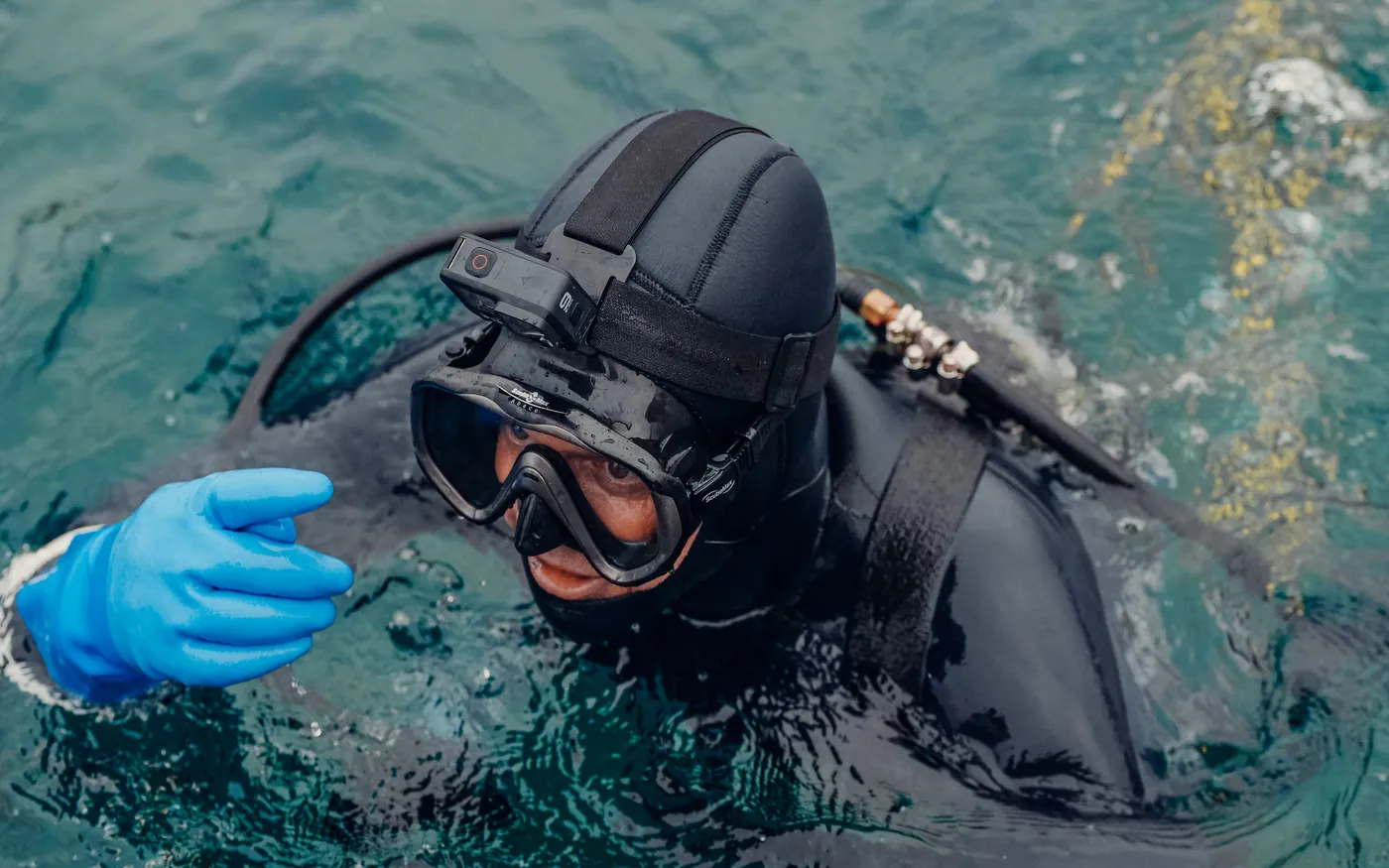 A hooded diver at the surface wearing thick gloves