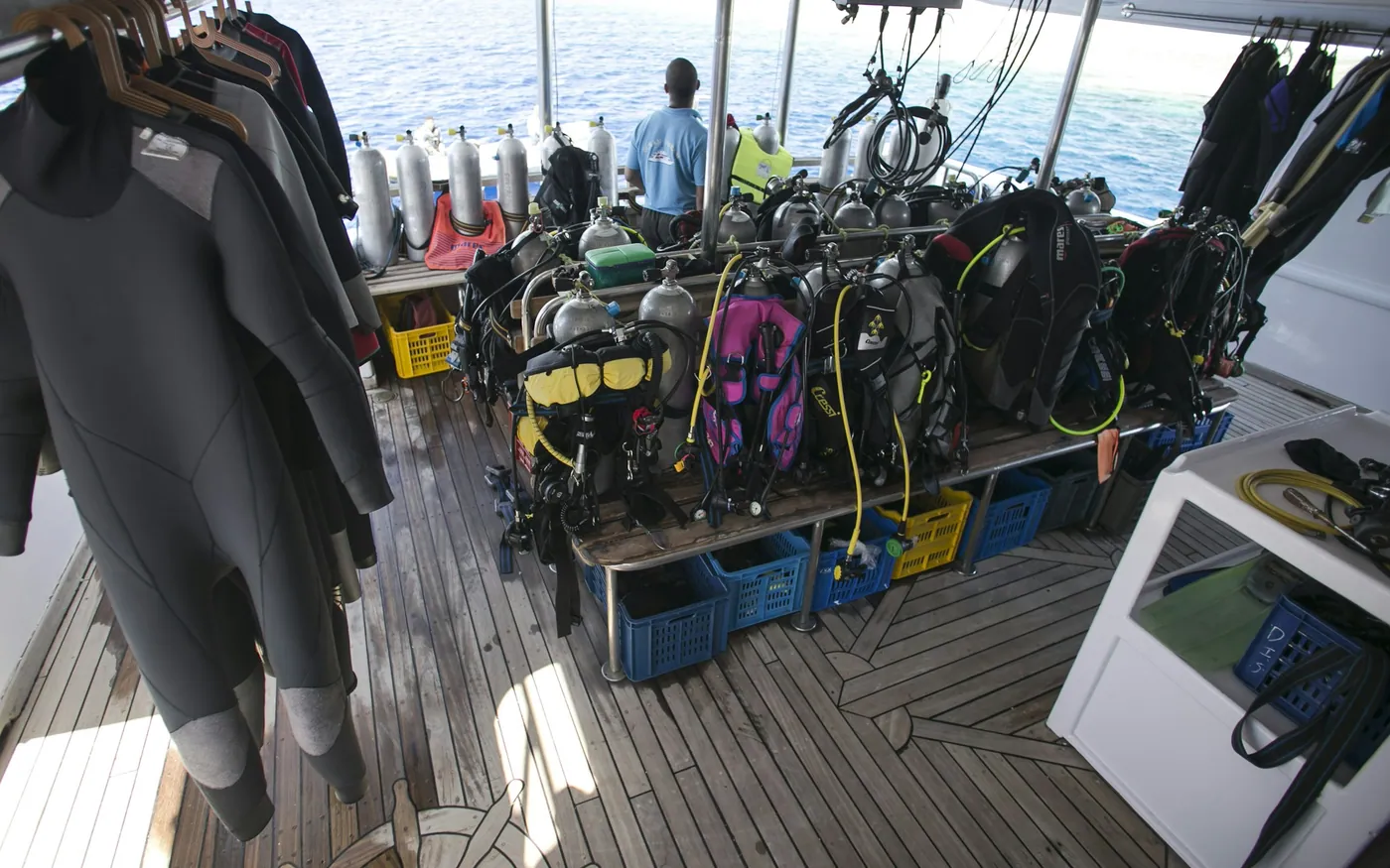 Rental wetsuits hanging above rows of BCDs and cylinders on a dive boat