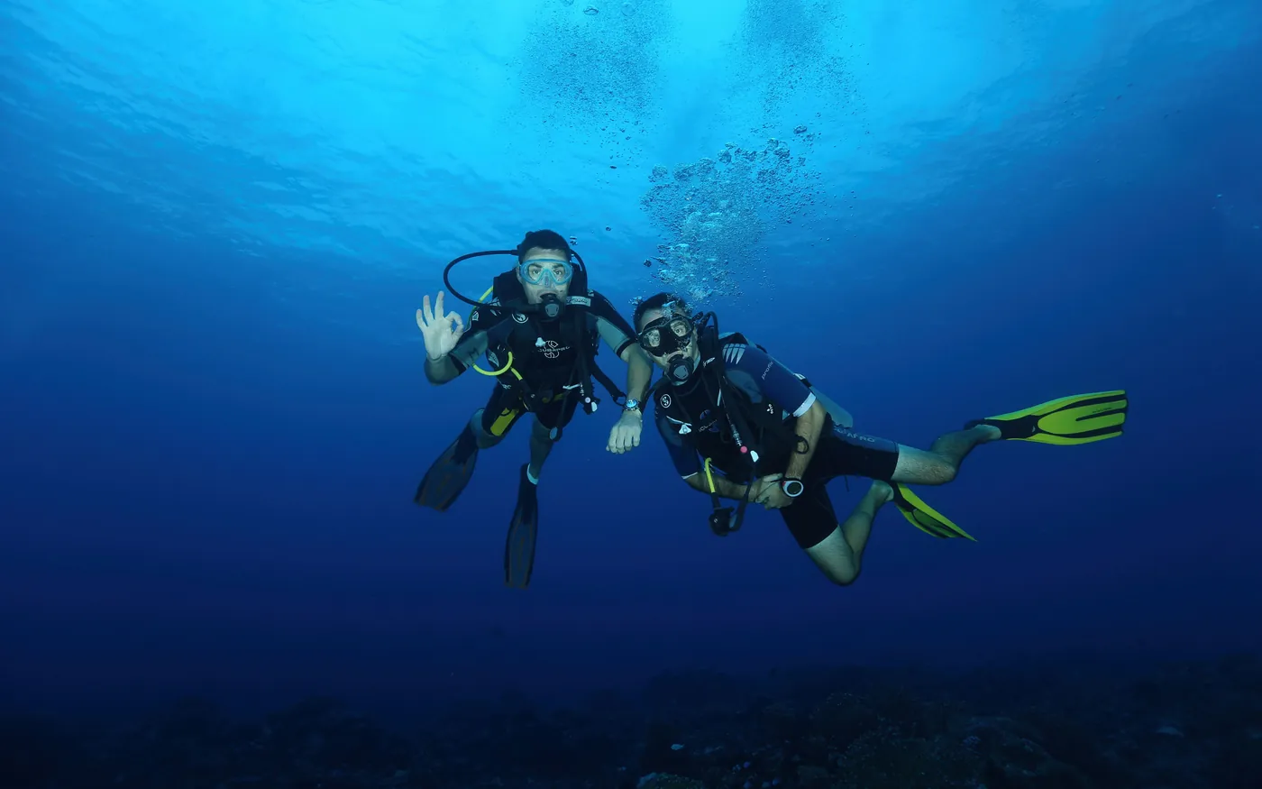 Two scuba divers side by side underwater, one signalling OK