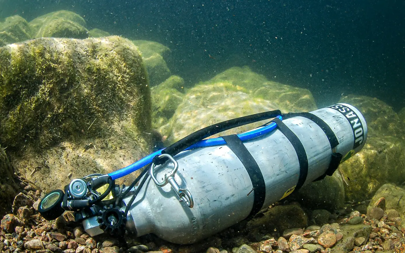 An aluminum scuba cylinder with a regulator attached resting on the seabed