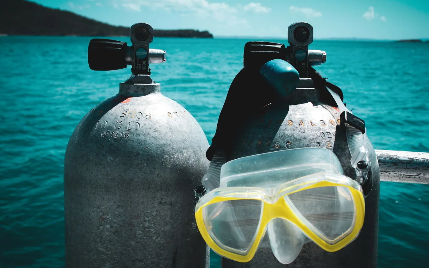 Two scuba cylinders standing on a boat with a yellow mask hanging from one