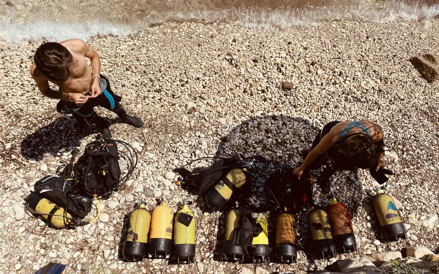Divers preparing several scuba cylinders laid out on a rocky shore
