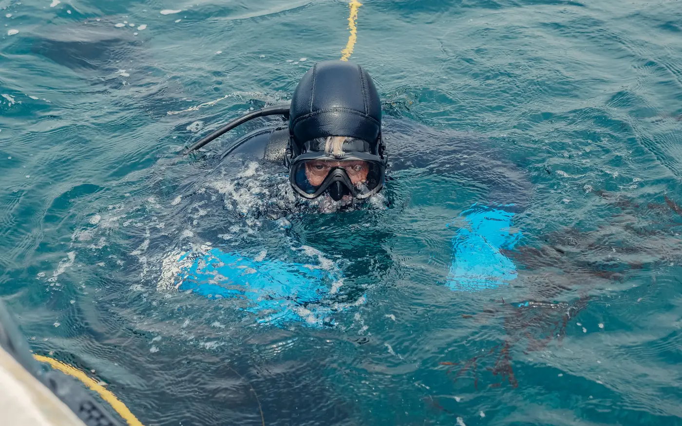 A scuba diver in a hooded wetsuit and mask at the surface, about to descend