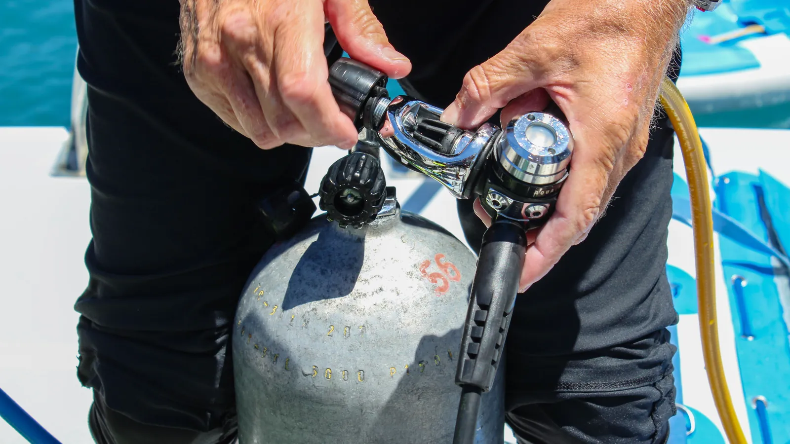 Hands attaching a scuba regulator first stage to the valve of an aluminum cylinder
