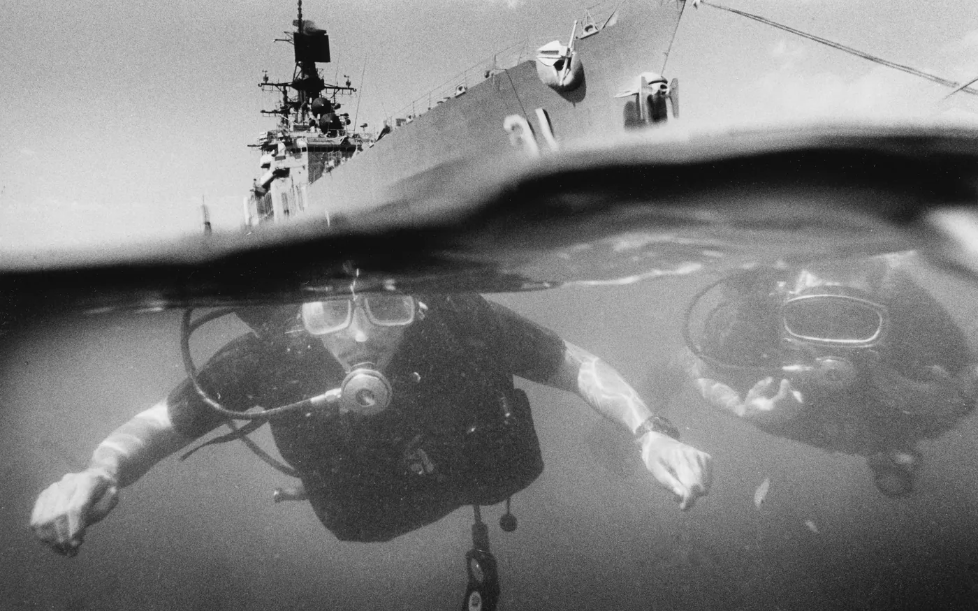 Two scuba divers at the surface beside the hull of a large ship