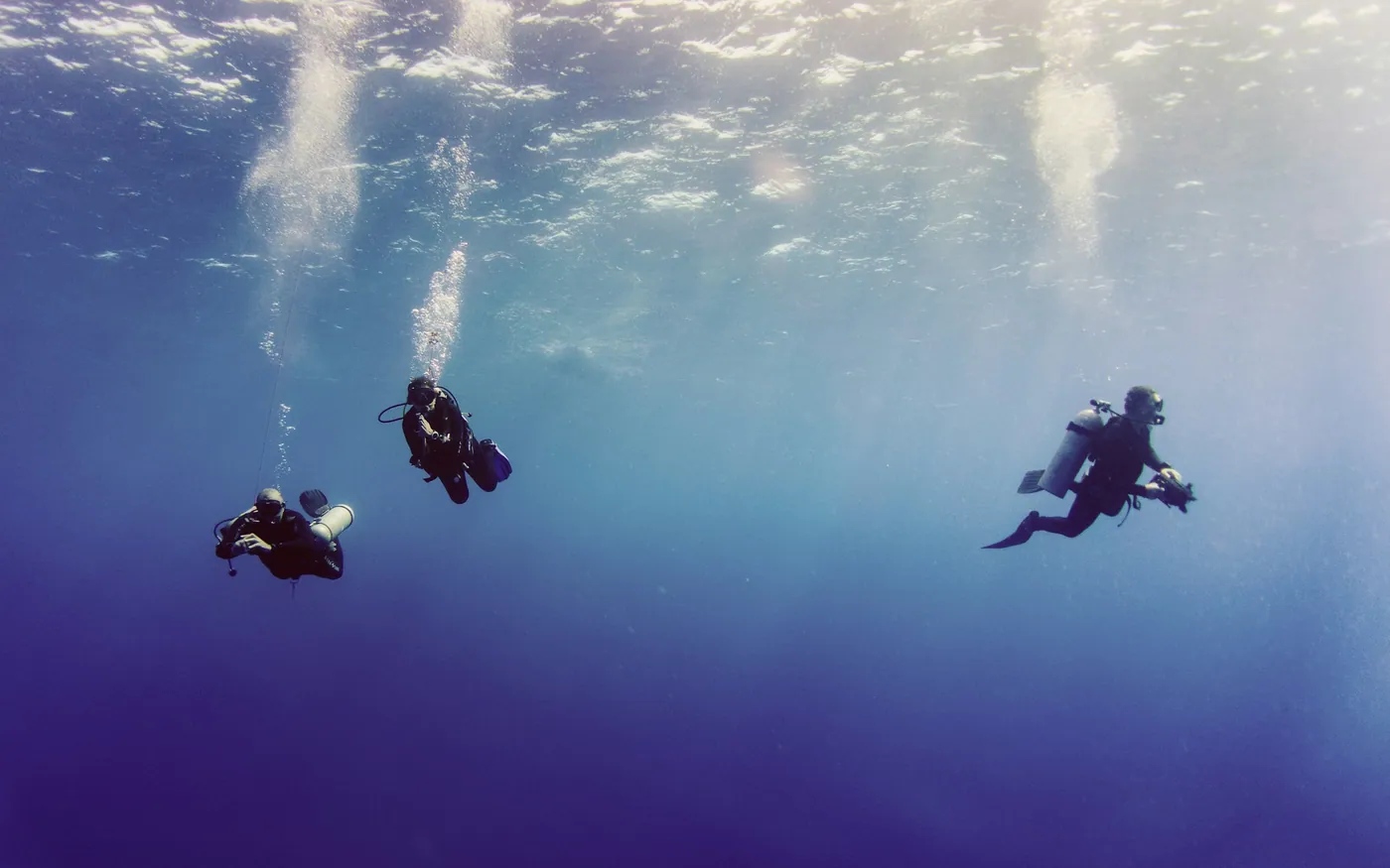Three scuba divers ascending together, each trailing bubbles